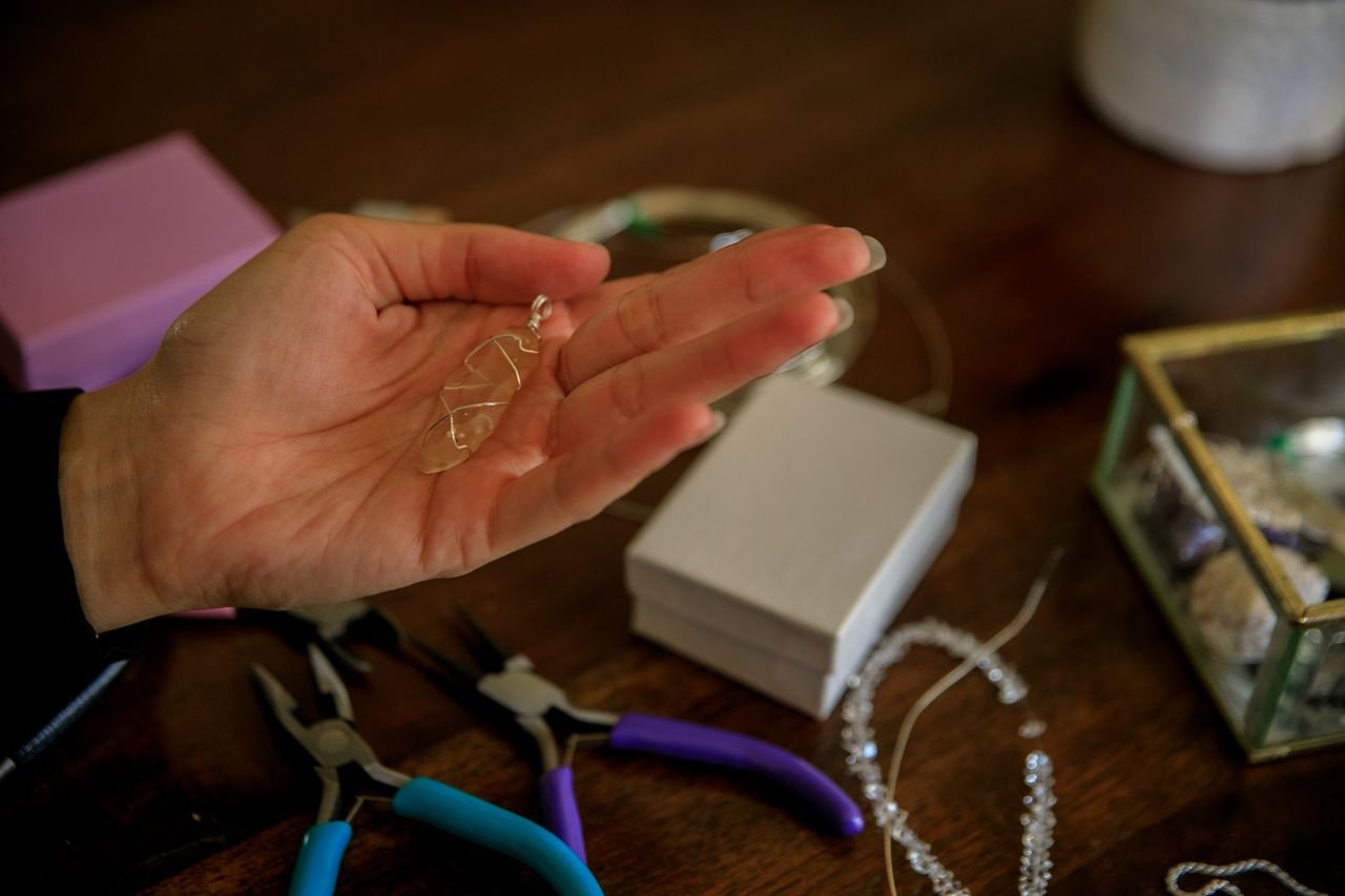 Close-up of a hand holding a crystal pendant surrounded by jewelry tools.