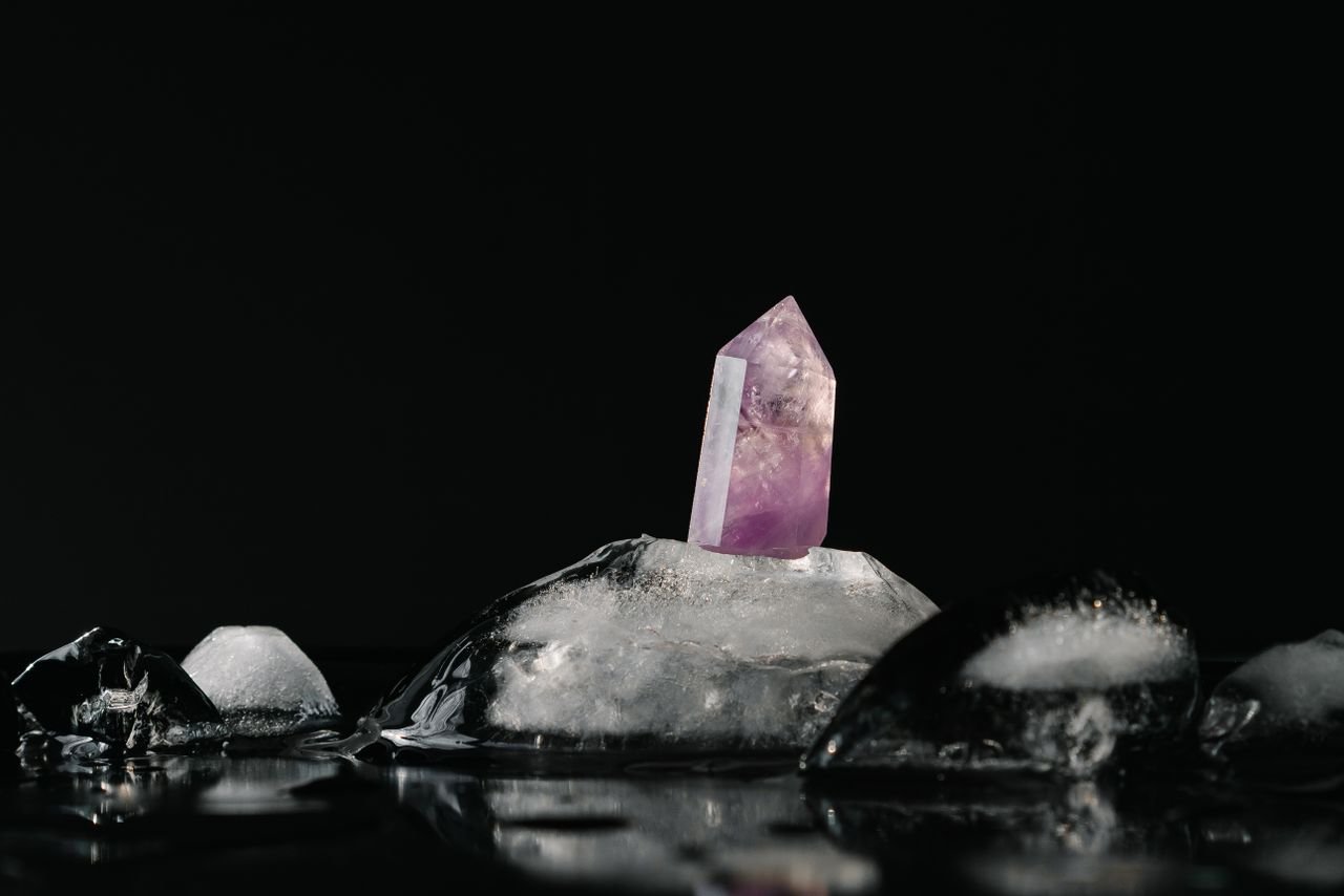 A vivid purple amethyst crystal surrounded by melting ice on a reflective black surface.